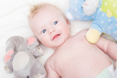 baby laying down in diaper with toys next to him