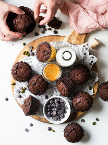 person-opening-chocolate-muffin-with-chocolate-chips-white-plate-with-muffins-coffe-and-milk-bottle