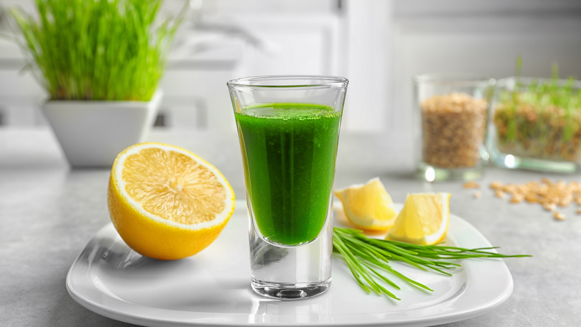 Energy elixir juice made with fresh wheatgrass, half a cucumber, green apple slices, and a squeeze of lime, served in a clear glass with a vibrant green color.