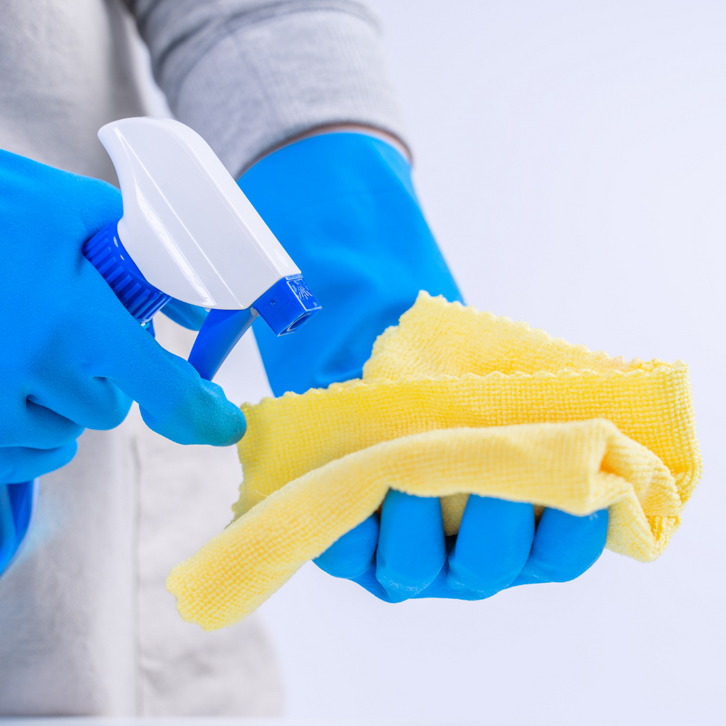 person with gloves spray bottle cleaning utensils and cloth spraying solution into cloth