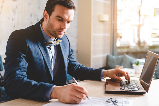smart businessman typing on a laptop and taking notes on paper at a desk