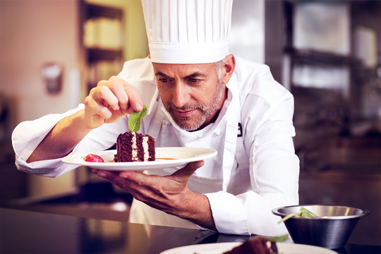 a male chef decorating a chocolate cake on a plate with mint