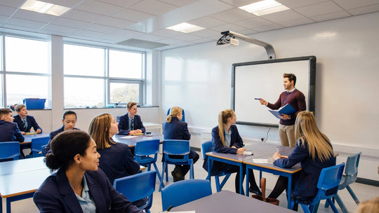 a male teacher speaking to a class of children in a school with the children wearing blazers and shirts