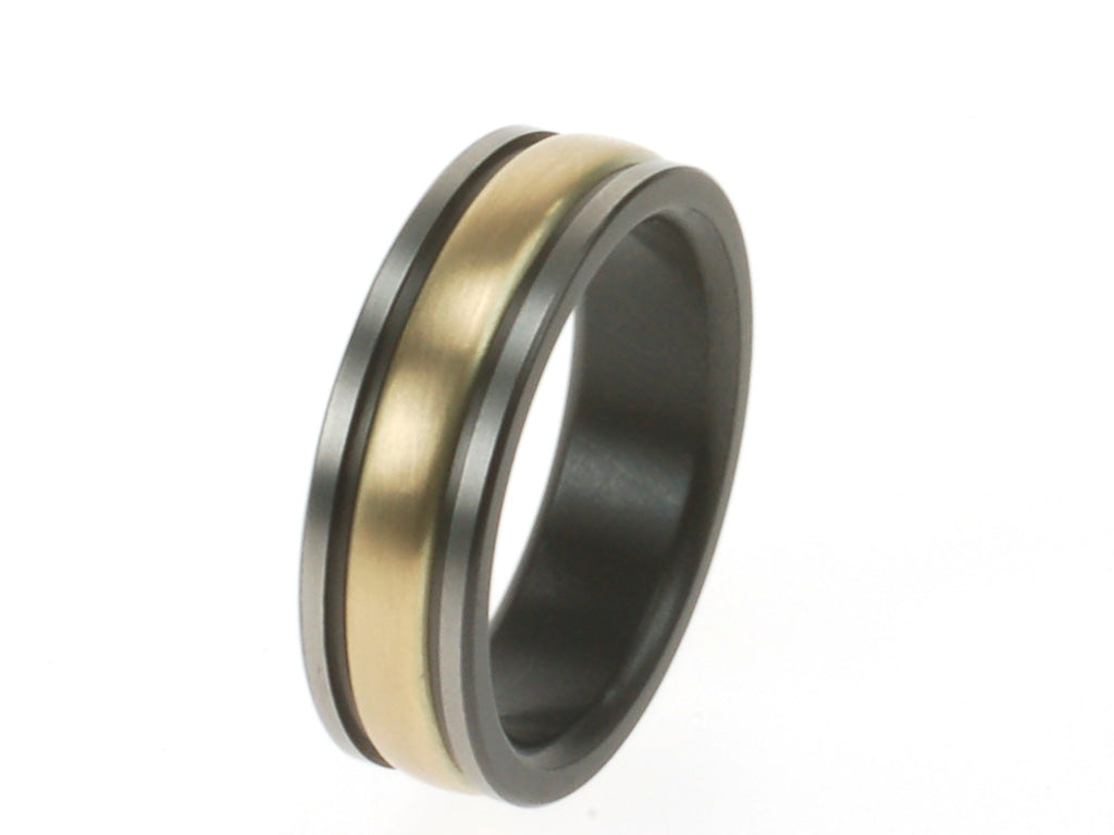 Herdenkingsring van titanium en zwart zirkonium met ruimte voor as, strak en krachtig van vorm.