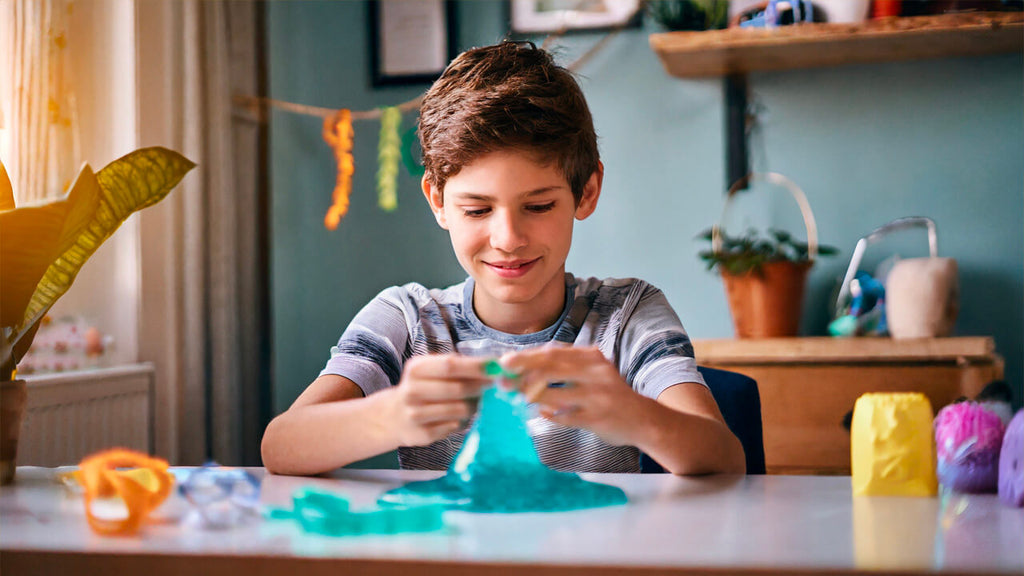 Boy is sitting at his desk in his bedroom, playing with slime for therapeutic benefits.