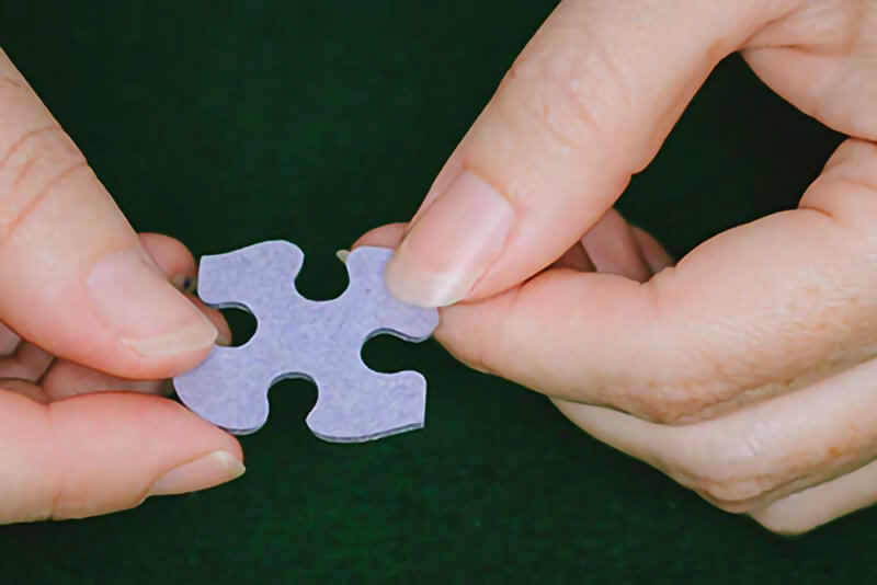 Person holding a White Mountain puzzles puzzle piece, which is made of blue chipboard.