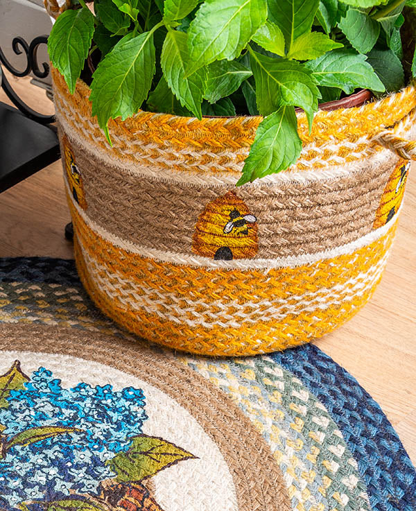 Braided basket with bee and beehive design as decorative plant holder.