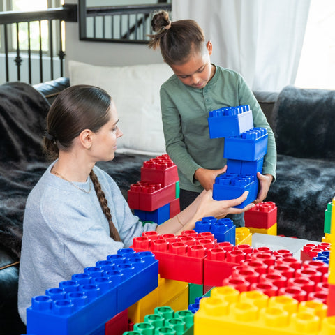 A child and an adult engage in creative indoor play, stacking extra large building blocks to build a fun structure together, showcasing the collaborative and imaginative possibilities of Biggo Blocks.