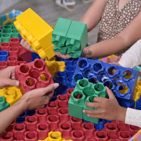 Children and an adult playing together with colorful extra large building blocks, focusing on hands-on learning and teamwork.