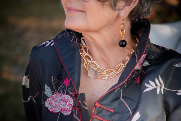 a closeup of a woman wearing a gold necklace and gold onyx earrings