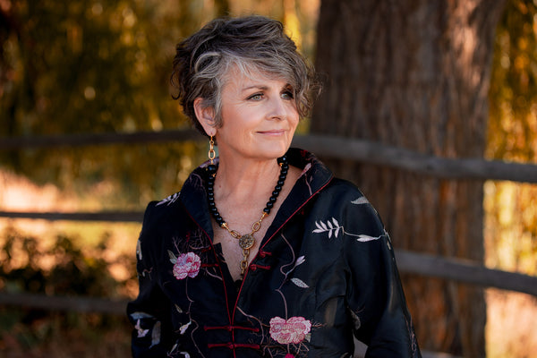 A woman in a jacket wearing a gold and black onyx necklace and pair of earrings