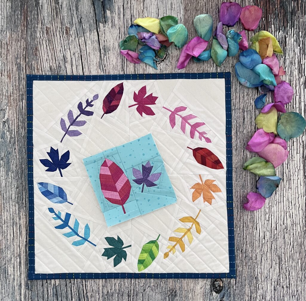 A mini quilt depicting a rainbow wreath of leaves, with a companion pattern showing two of the leaf patterns
