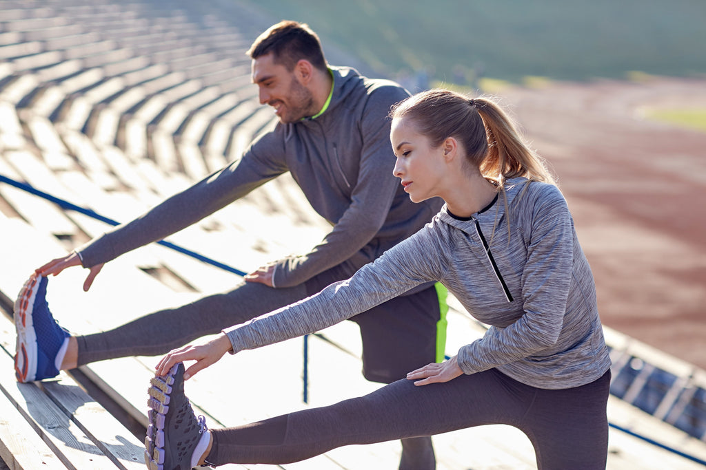 image of a male and female stretching on bleachers on a track 