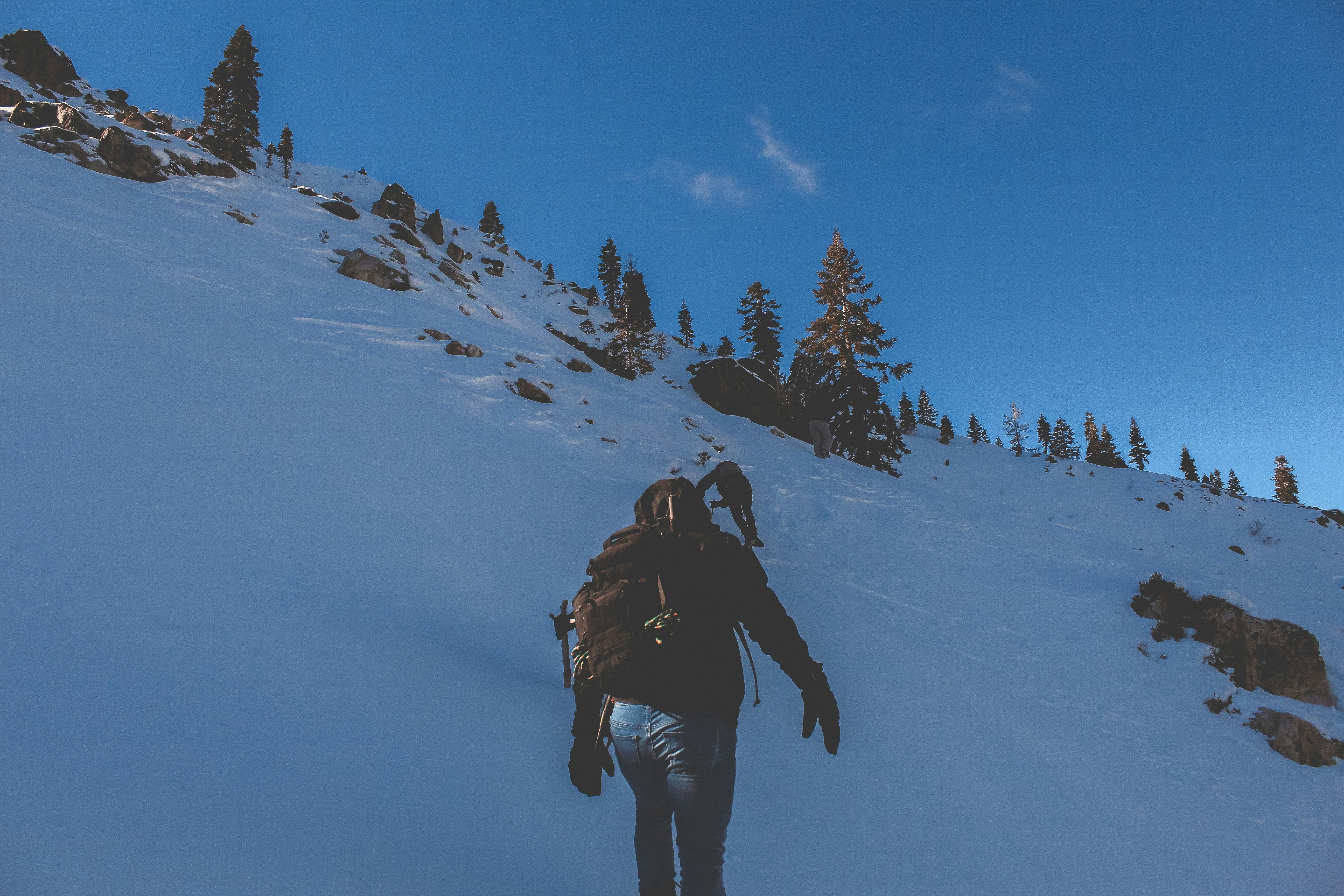 Person with a backpack trekking up a snowy mountain slope under a clear blue sky.
