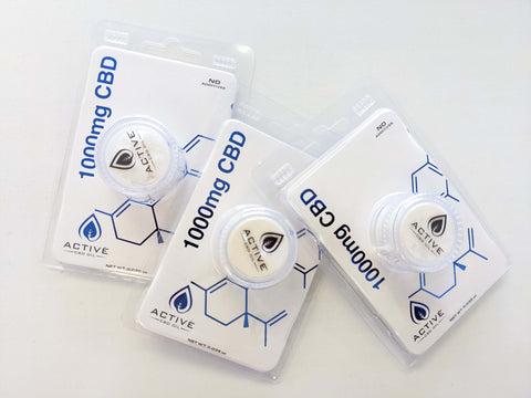 Three packages of Active CBD Oil 1000mg CBD Isolate Powder are pictured, edges overlapping. Each package contains a round, clear plastic container with white CBD isolate powder inside, a paper insert that has a white background with the molecular structure of CBD in blue print on the bottom right side of the paper, in a plastic clamshell package one a white background.