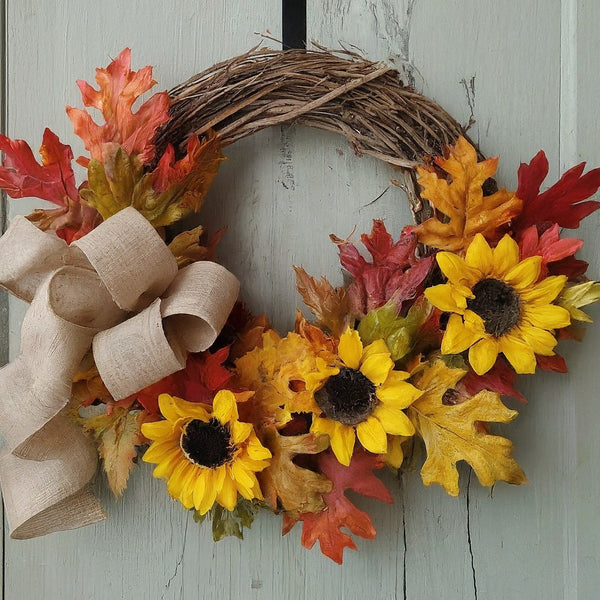 A DIY fall wreath with a grapevine base, colorful leaves, burlap ribbon, and a cluster of faux sunflowers