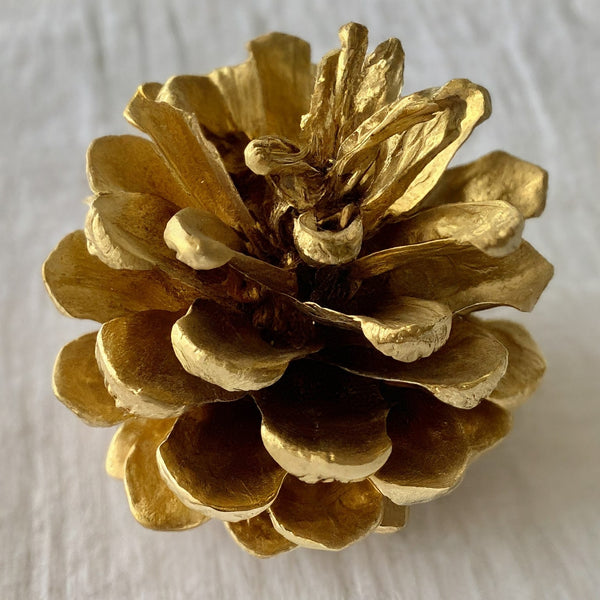 Gold-painted pinecones nestled among natural acorns and dried fall leaves on a white tablecloth