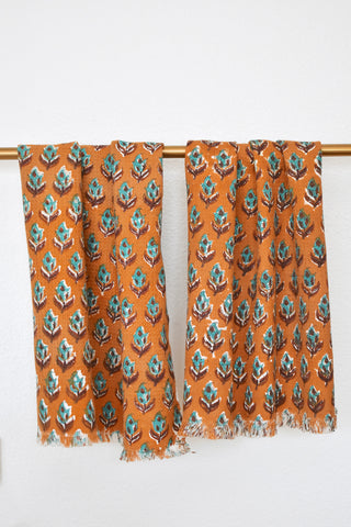 Two floral printed hand towels hanging on a gold rod. Towels have an orange background and a teal floral print.