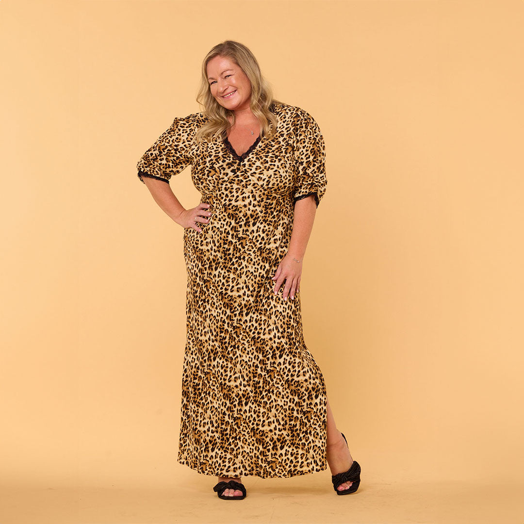 Woman in leopard print dress smiling against a beige background.