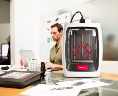 A man works on a laptop next to a 3D printer