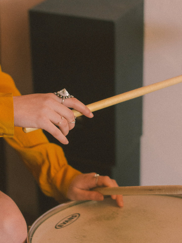 GIRL IN BAND PLAYING THE DRUMS IN STATEMENT CRYSTAL GEMSTONE RINGS AND MUSTARD CHLOE SILK SHIRT 