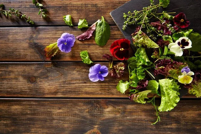 A view of edible flowers and salad greens on a wooden table.