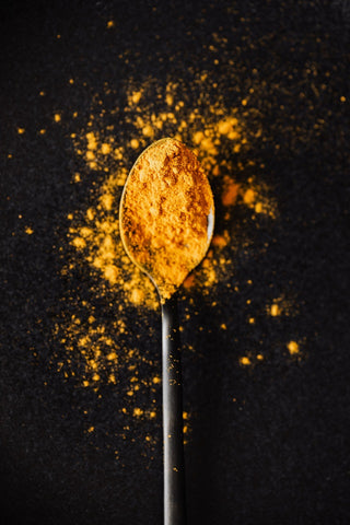 Curcuma powder on tablespoon and spilled on black surface