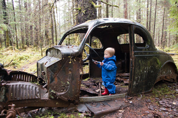 Small boy wearing blue waterproof gear explores abandoned car in rural Alaska