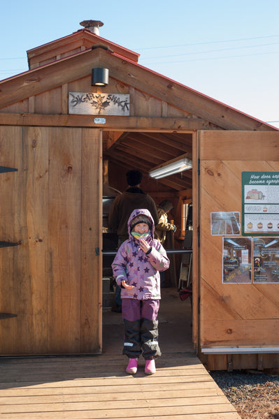 child in villervalla snow gear in front of a maple sugar house