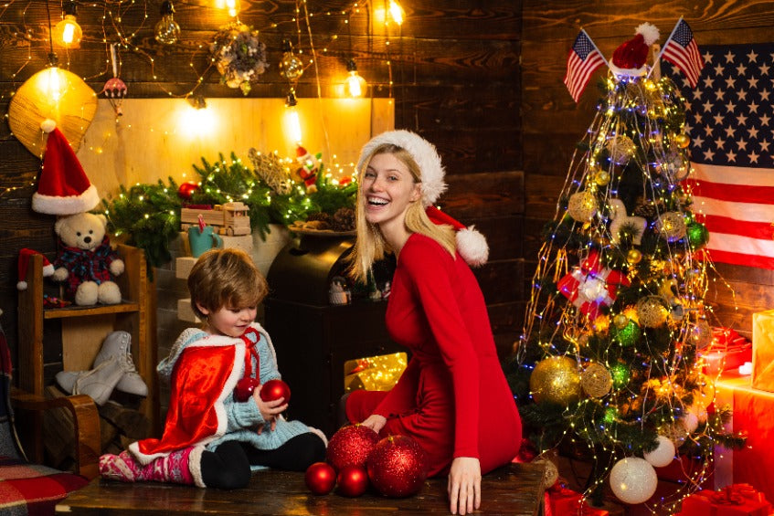Une maman en robe rouge et son enfant devant un sapin de Noël décoré, ambiance festive et joyeuse à la maison.