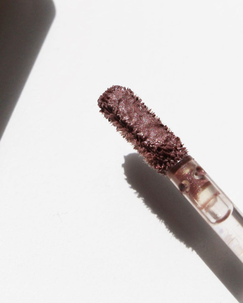 ILIA Beauty Eye Tint in the color Dim. On the image is its doe foot applicator, an up close. This is a lavender color with purple and pink pearl. Metallic finish.