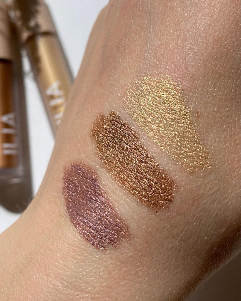 Hand swatches of eyeshadows. From top to bottom are: Gleam, an antique gold color, then Sheen, a copper bronze and Dim, Gray, a lavender with pink and purple pearl. These are Eye Tints, liquid eyeshadow that turn from cream to powder, by ILIA Beauty.