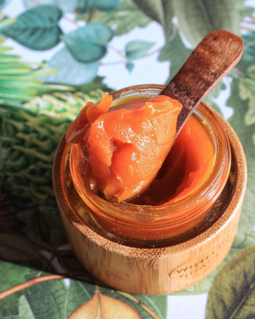 deep and rich orange face balm on a wooden spoon placed on the jar. this is mahalo the winter grace balm