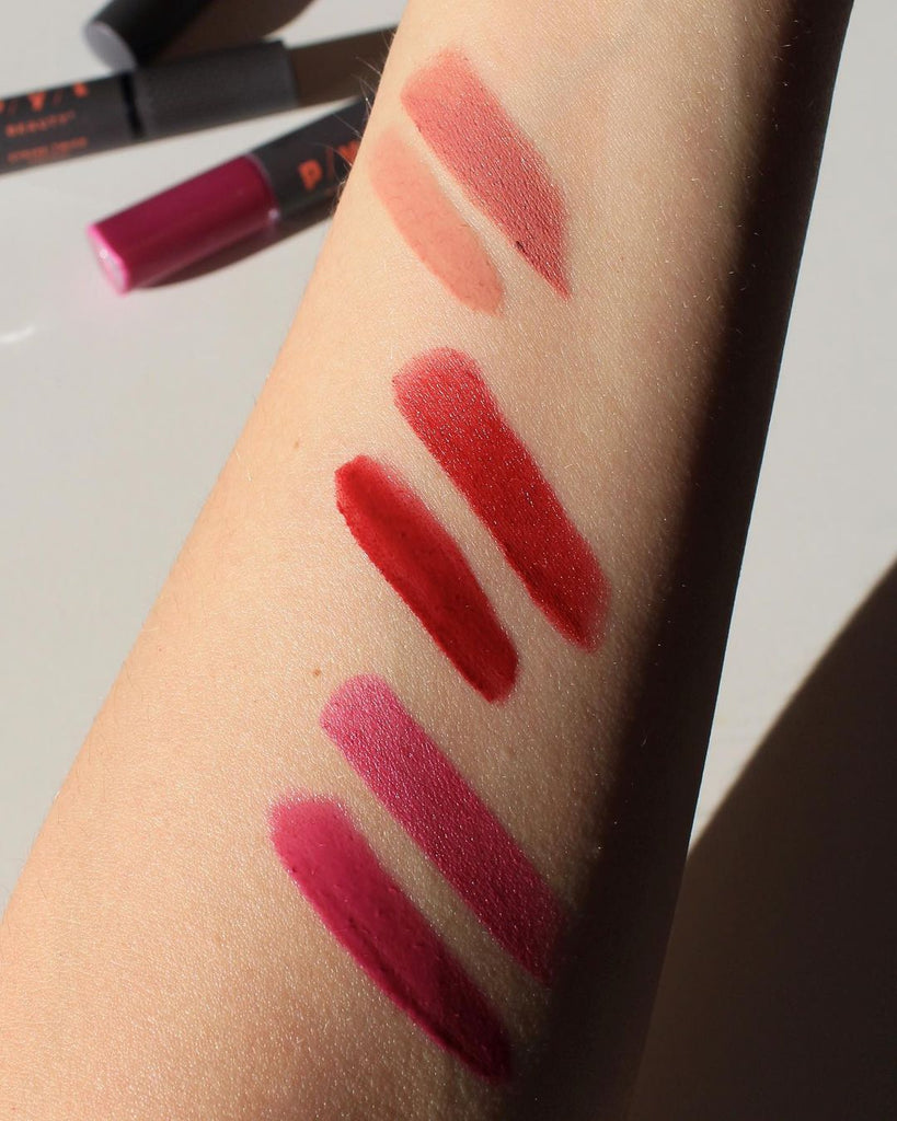 Hand lip swatches. Three lipsticks and three lip glosses in vibrant and bright colors. From top to bottom are a neutral nude shade called Icon, then it's a more dark red shade called Tell All and the last is the shade called Legit, which is a fuchsia color. These are Double Duty Lipstick + Gloss by PYT Beauty.