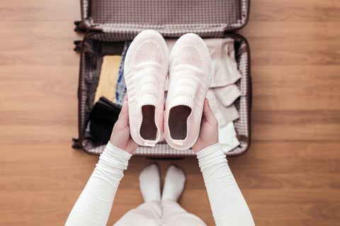 Top view of woman packing travel shoes in her suitcase