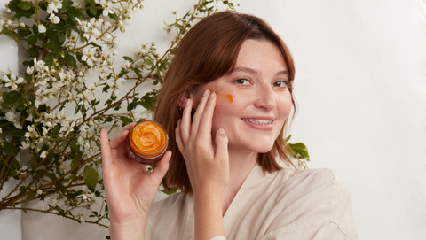 woman smiling as she puts on a face balm