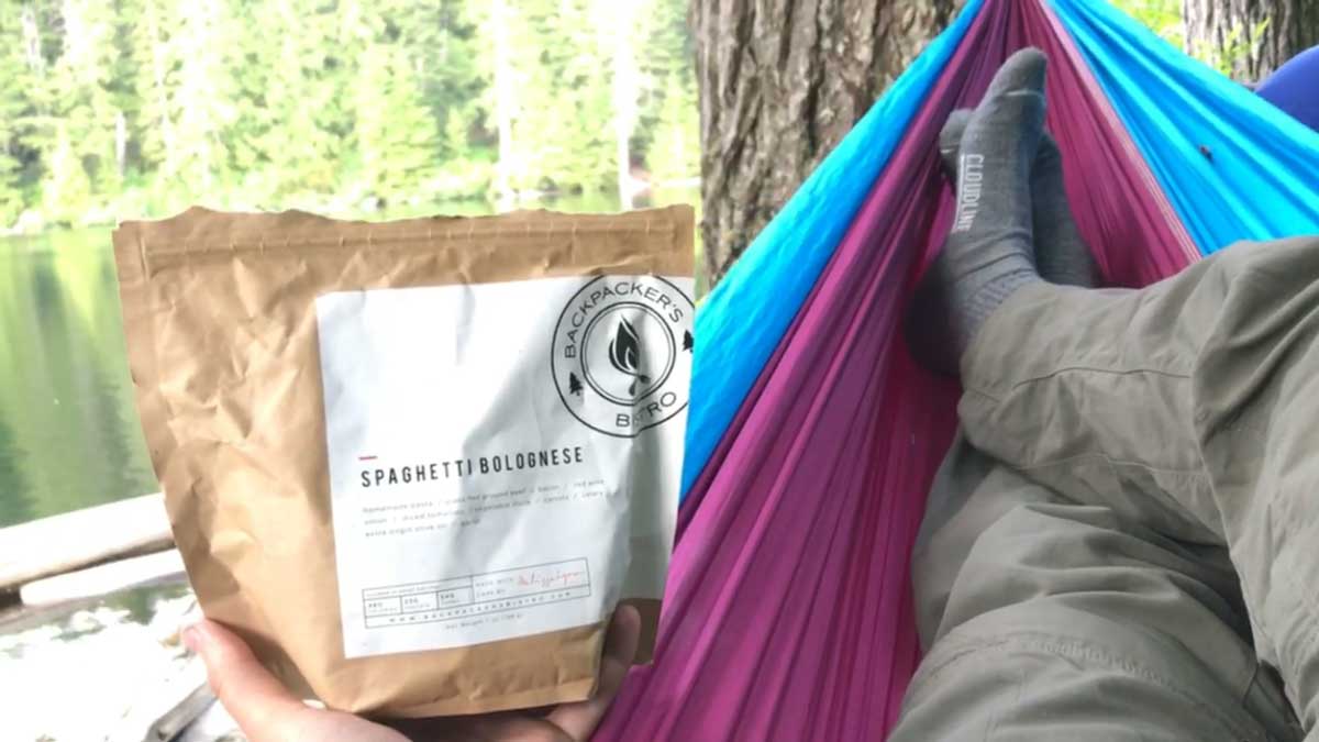 Backpacker wearing Cloudline socks and holding dinner pouch laying in hammock.