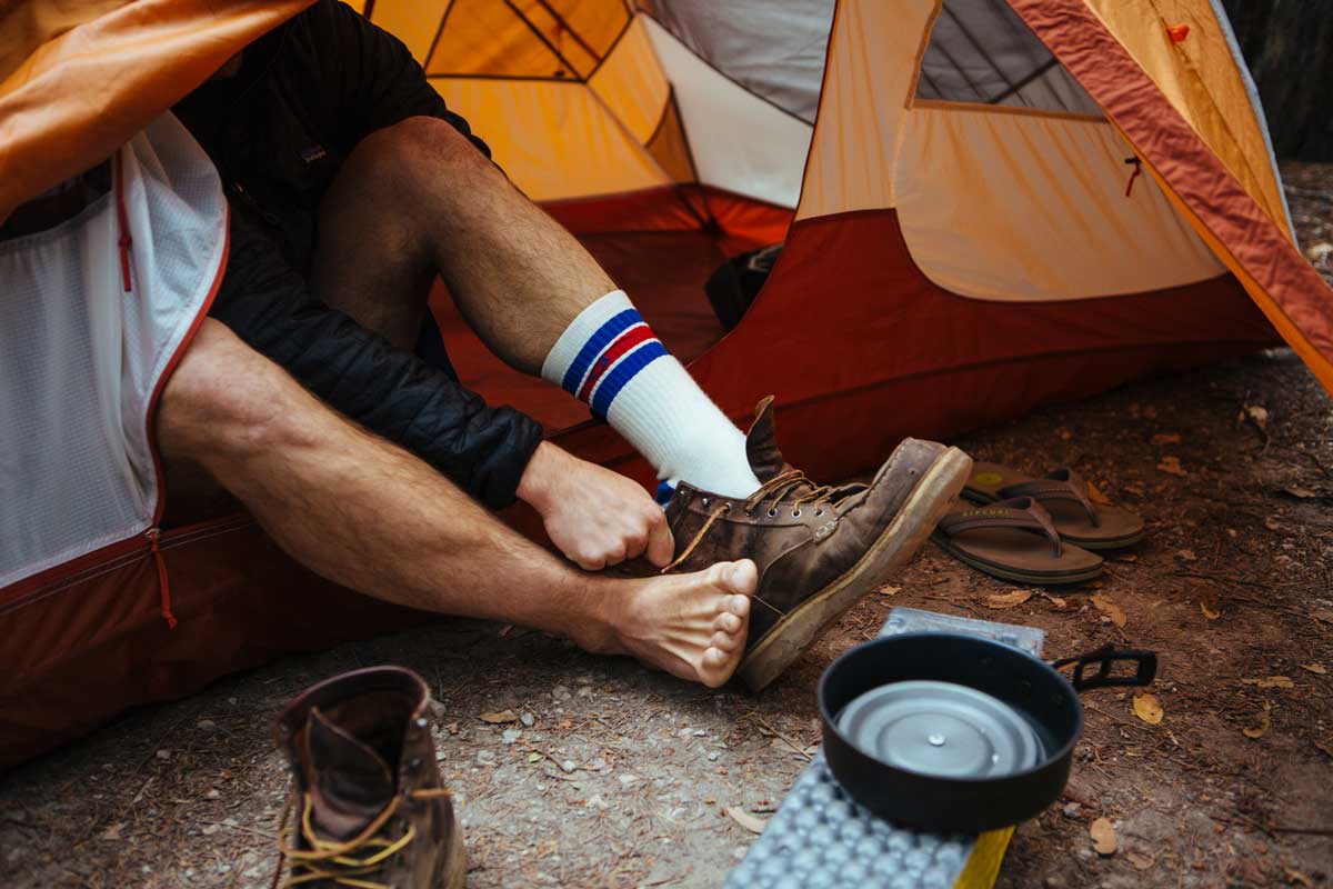Man sitting half in tent with feet out while putting on Cloudline hiking socks.