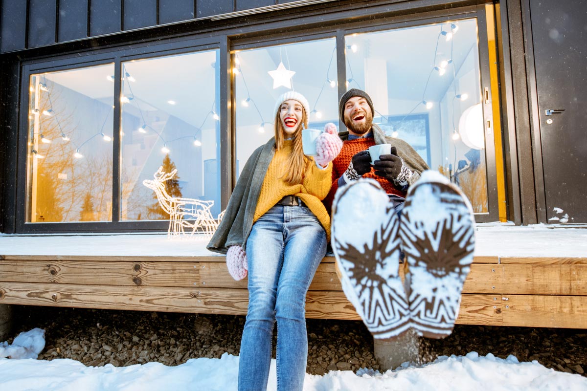 Winter retreat: Couple cozying up with hot cocoa outside a cabin for warmth.