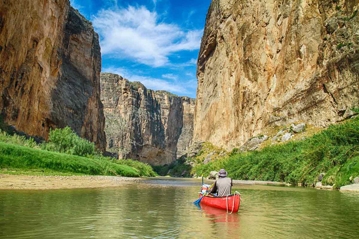 Man paddling down a river in a red canoe at Big Bend National Park in winter.