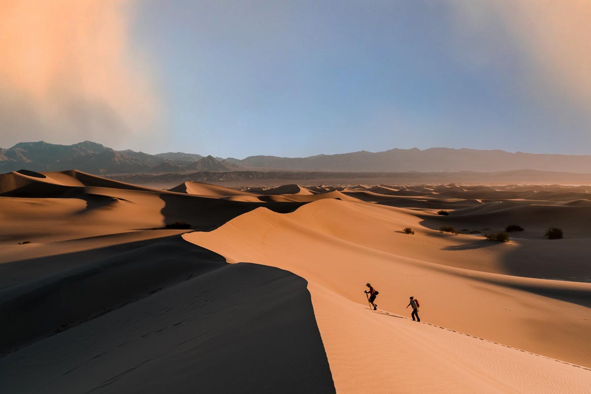Two hikers trekking up the sand dunes in Death Valley National Park.