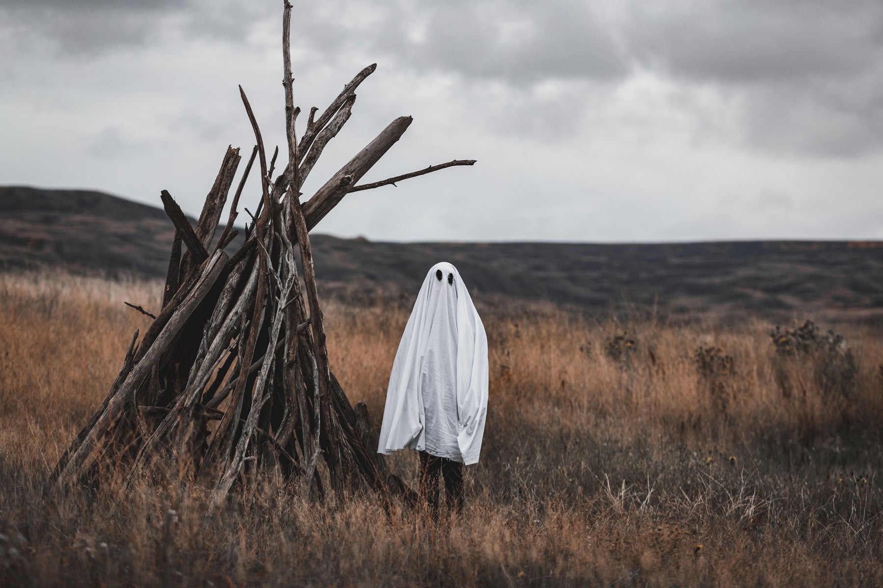 Hiker in ghost costume standing next to a spooky wooden shelter.