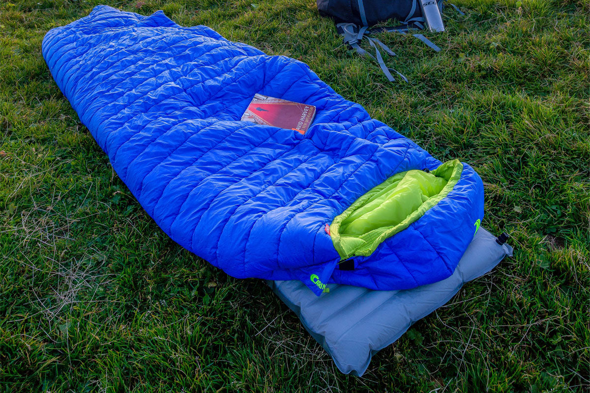 Inflatable sleeping pad with sleeping bag laid on top of it in the grass.