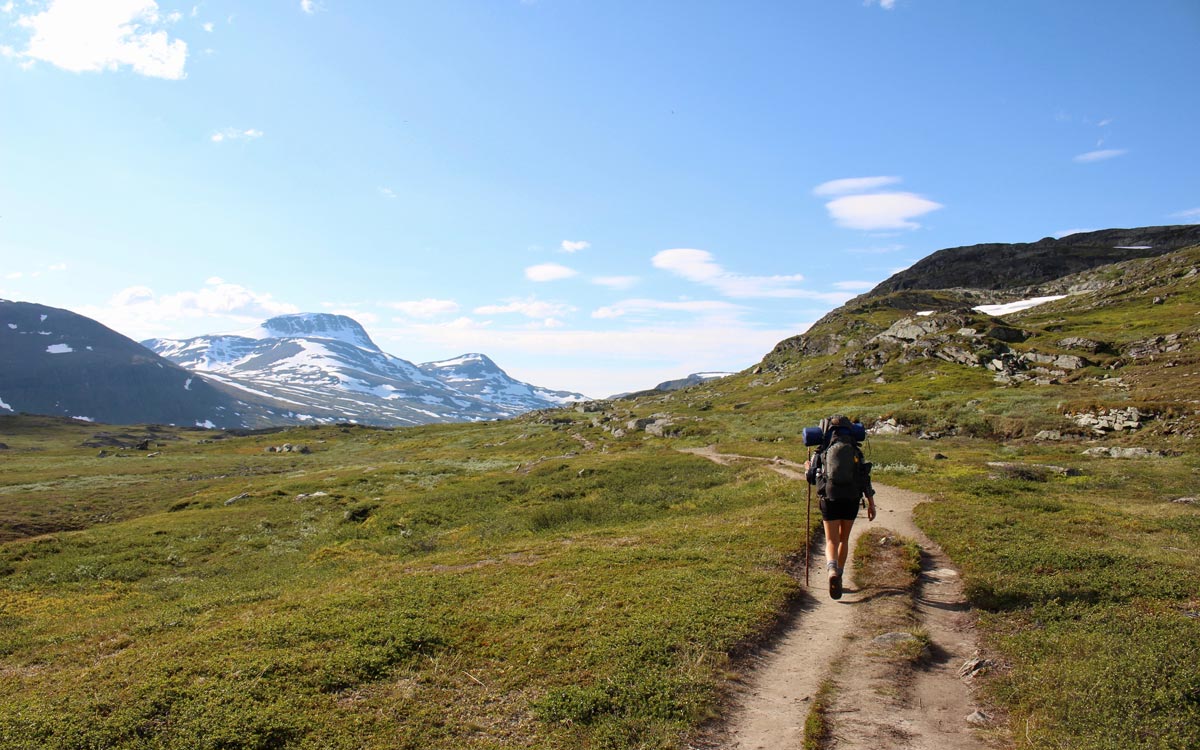 Backpacker hiking uphill towards snow peaked mountain.