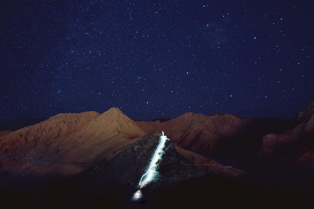 Starry night hike: Hiker's light trail captured in long exposure shot.