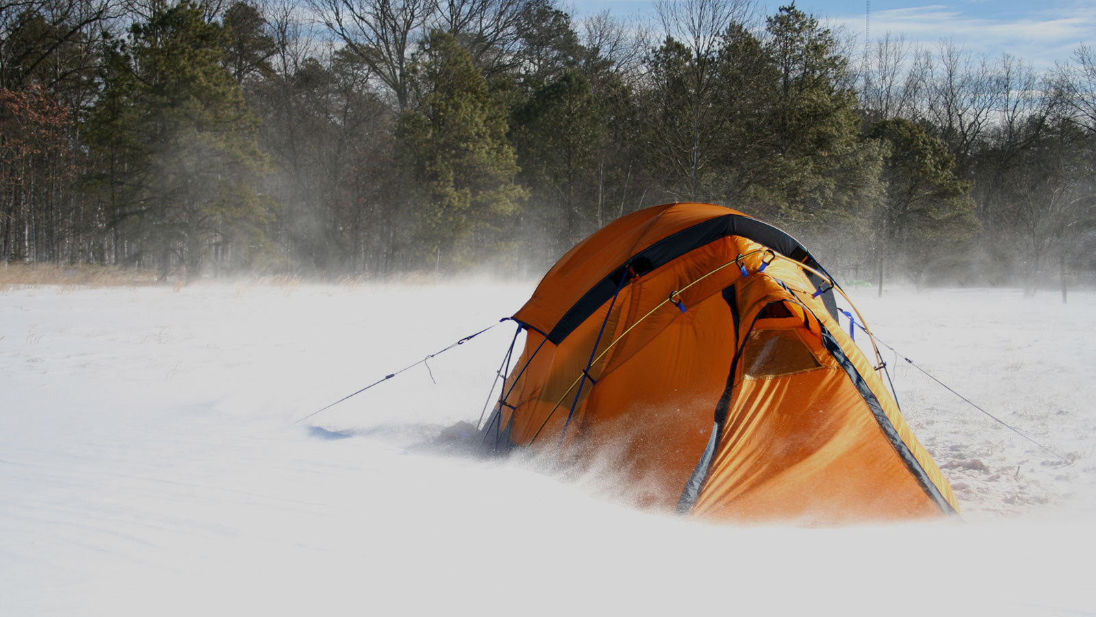 Orange tent on the snowy forest ground.