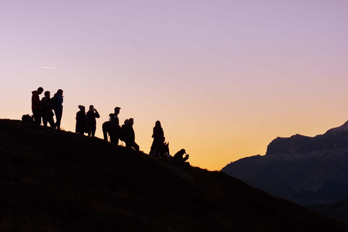 Group of friends on mountainside enjoying a colorful sunset.