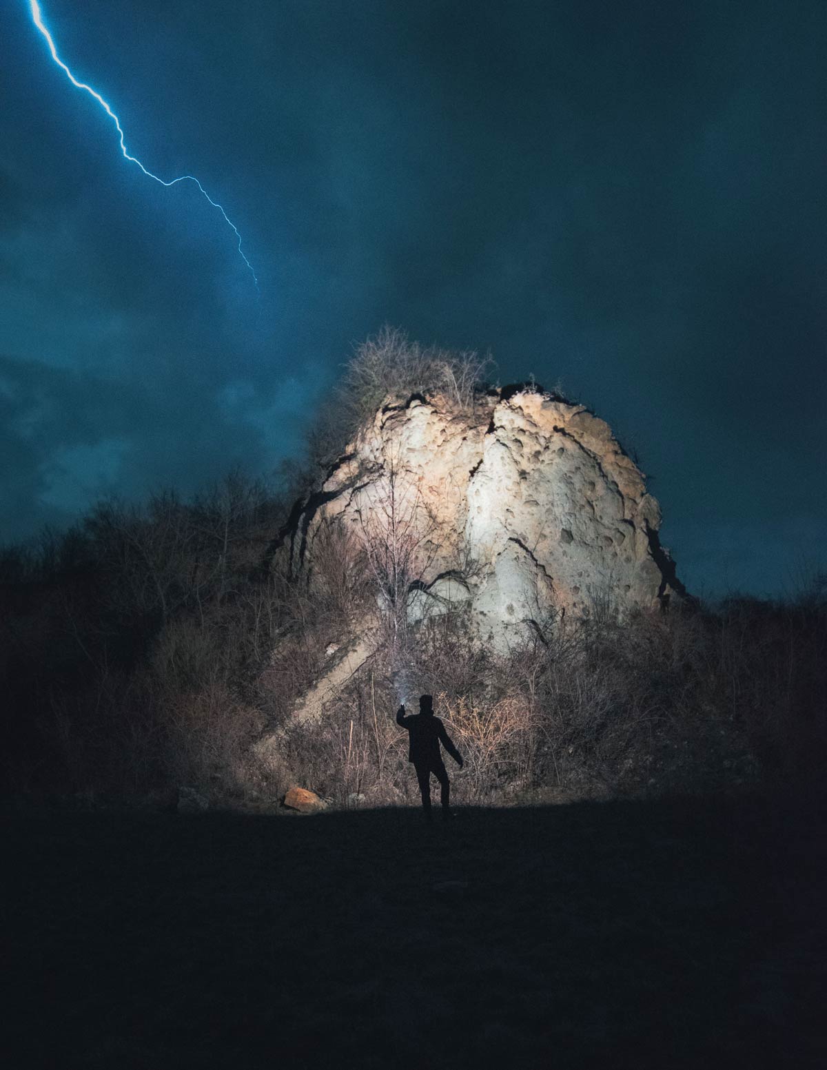 Hiker in lightning storm in front of mountain.