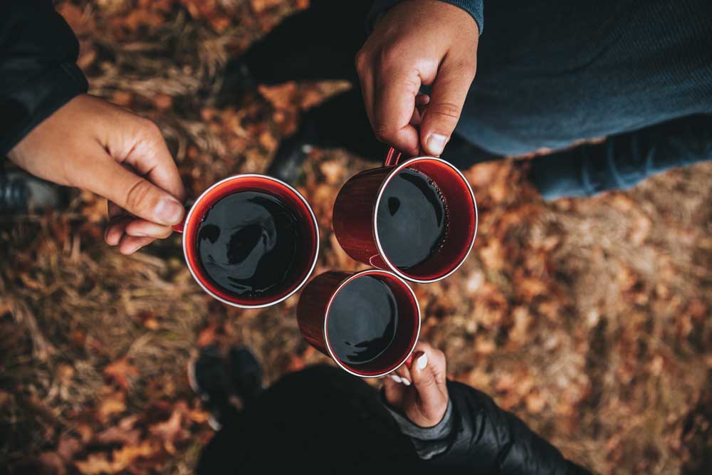 3 campers holding together their camp mug full of coffee.