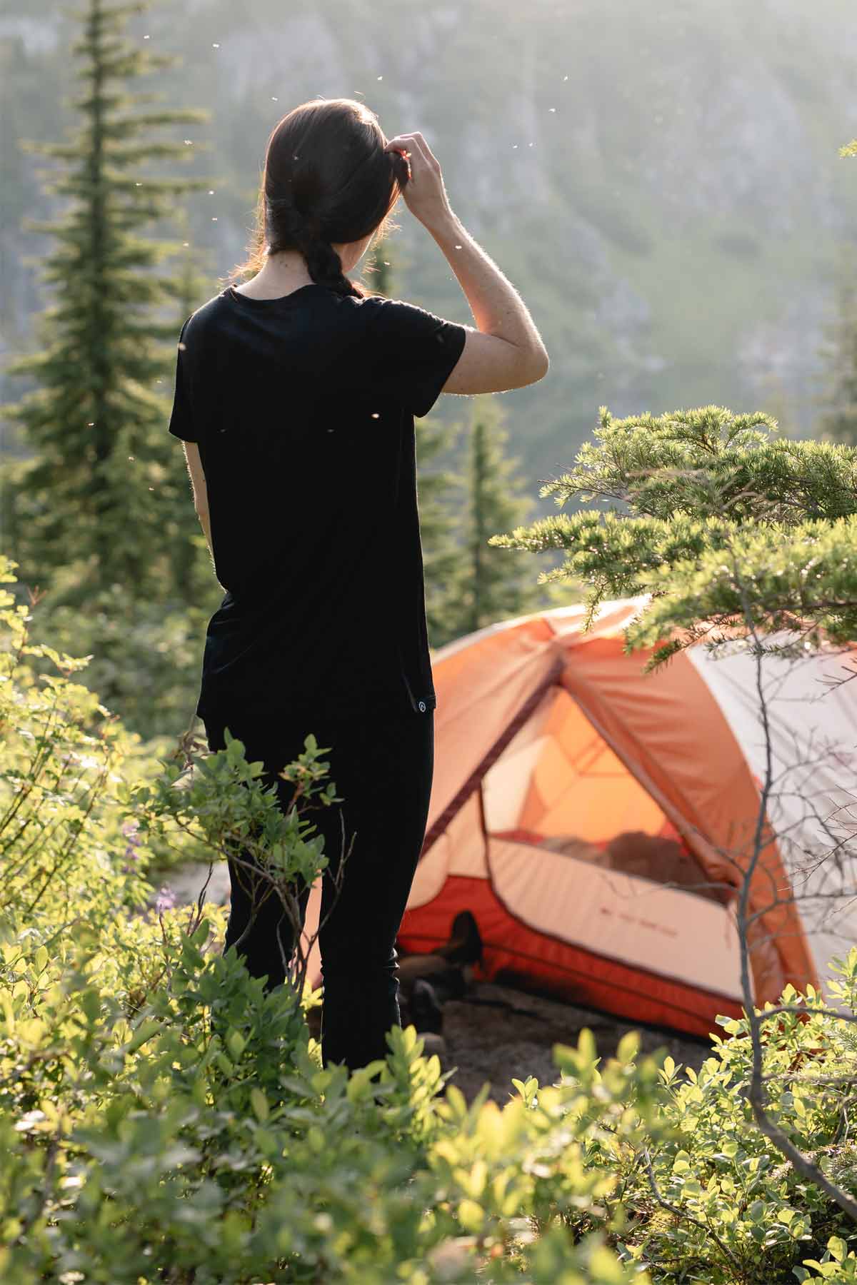 Backpacker standing outside a tent surrounded by a visible swarm of mosquitos.